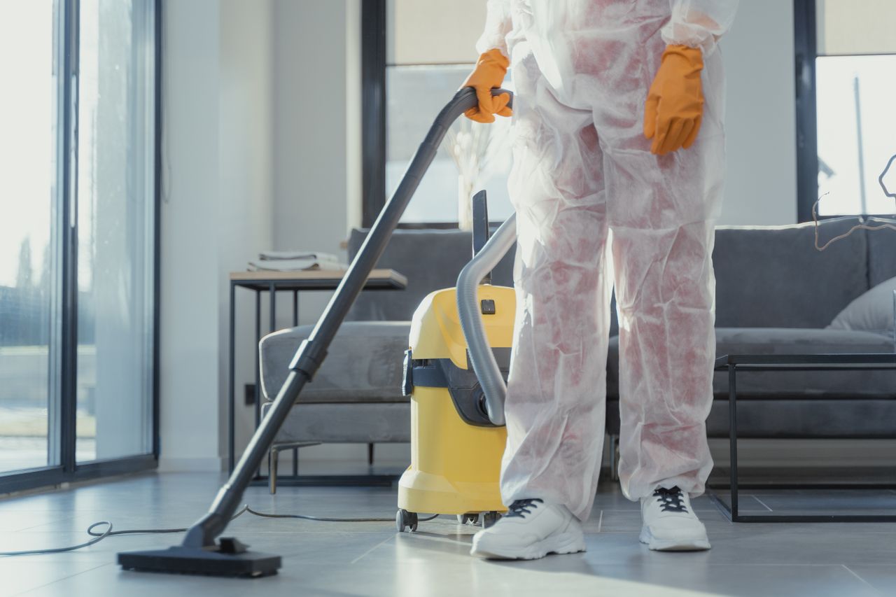 journey A cleaner in protective coveralls and gloves vacuuming a modern living room.